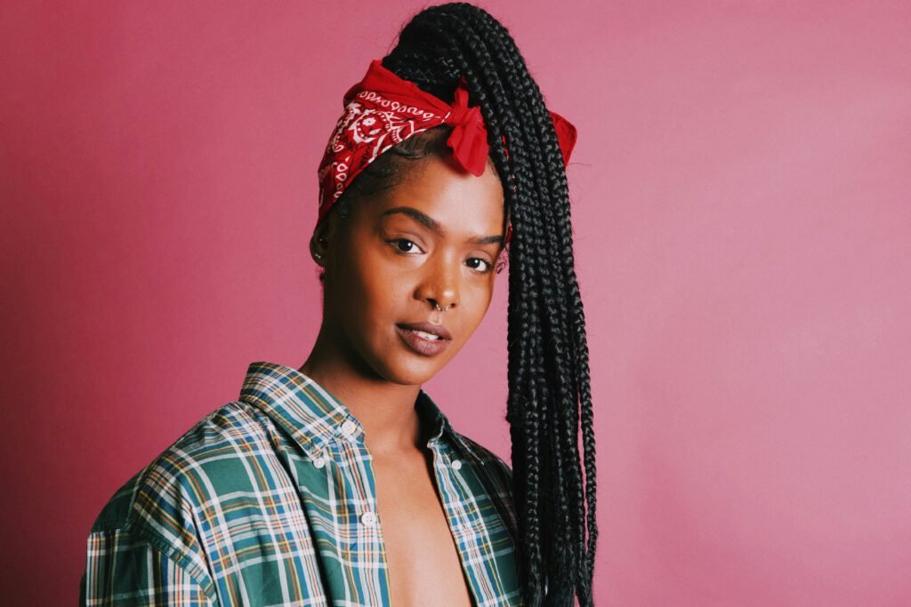 pexels-photo-1006202-1006202 Elegantly posed young woman with braided hair and plaid shirt against a pink background.