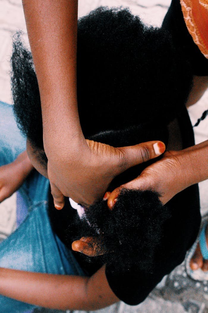 A close-up high angle view of two people braiding afro hair, emphasizing detail and texture.